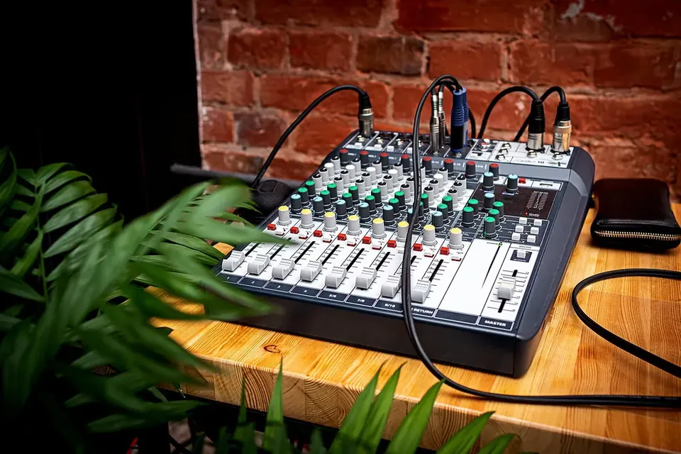 A compact audio mixing desk with rows of knobs and faders on a wooden shelf