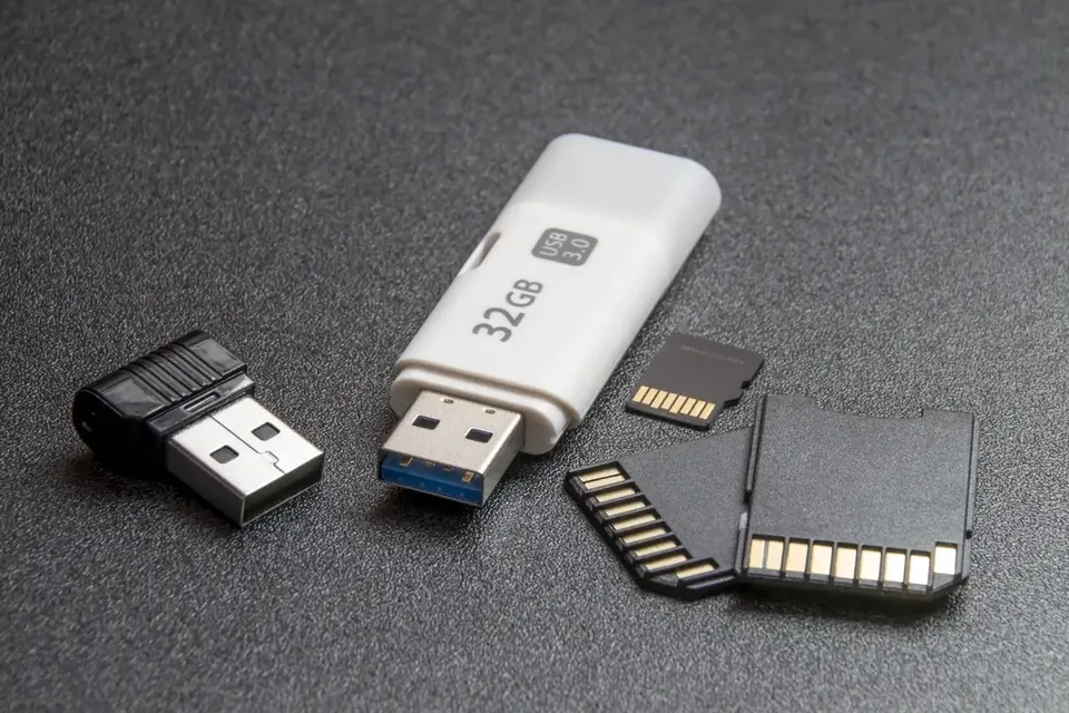 A white USB stick, a small black USB drive and three memory cards on a grey surface