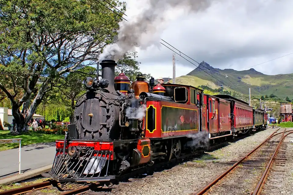 A black and red steam locomotive pulling carriages out of a country station