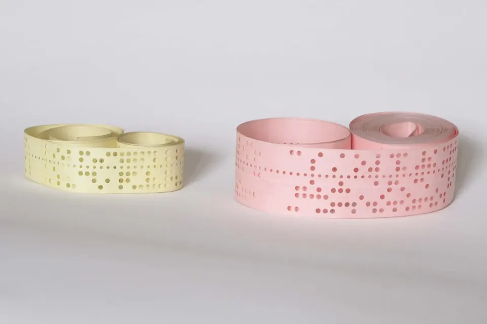 Two coils of punched paper tape, one yellow and one pink, on a white background