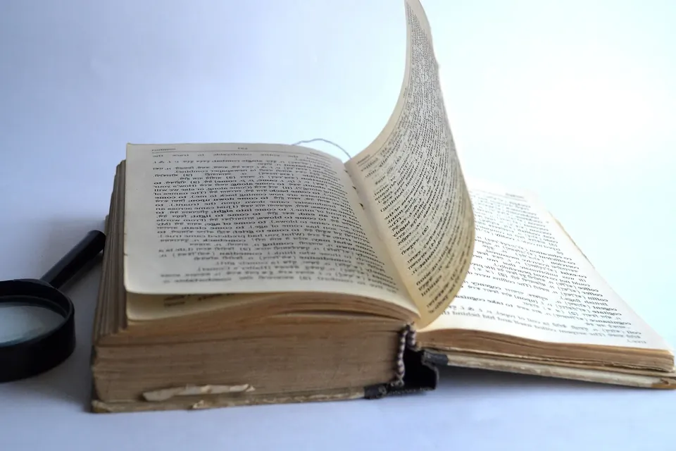 An old book lying open with one page lifting in mid-turn, a magnifier beside it