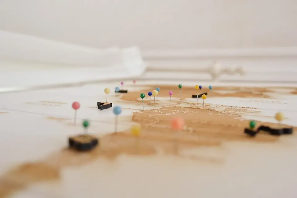 Coloured map pins stuck into a wooden world map, seen at table height with a shallow focus