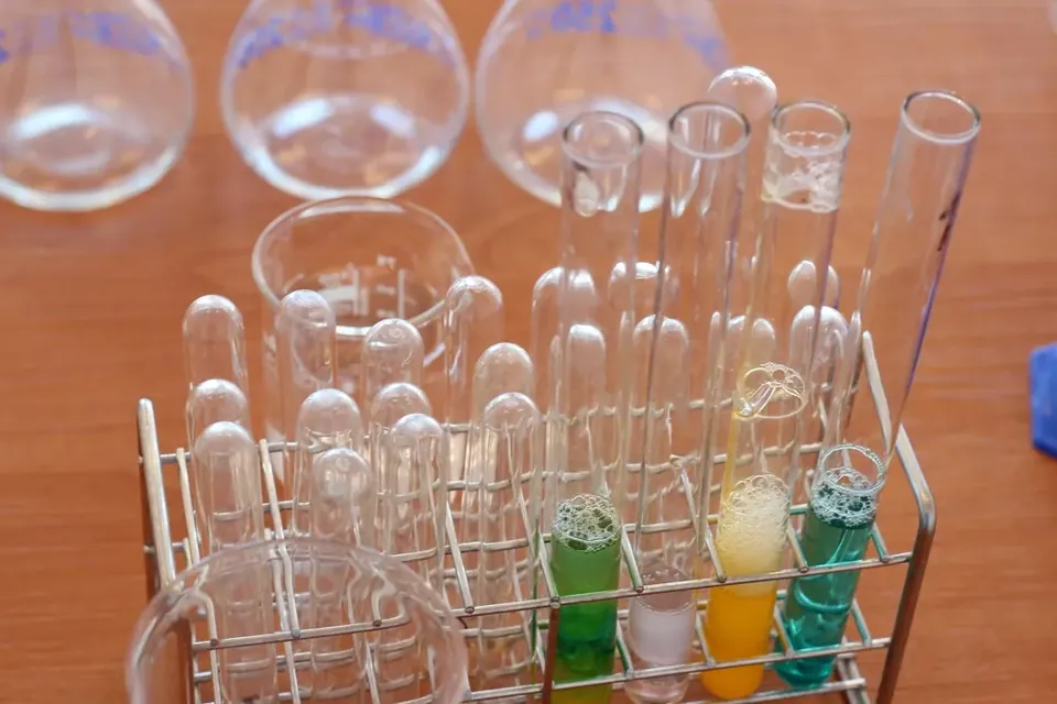 Glass test tubes in a metal rack, a few holding green, yellow and blue liquids