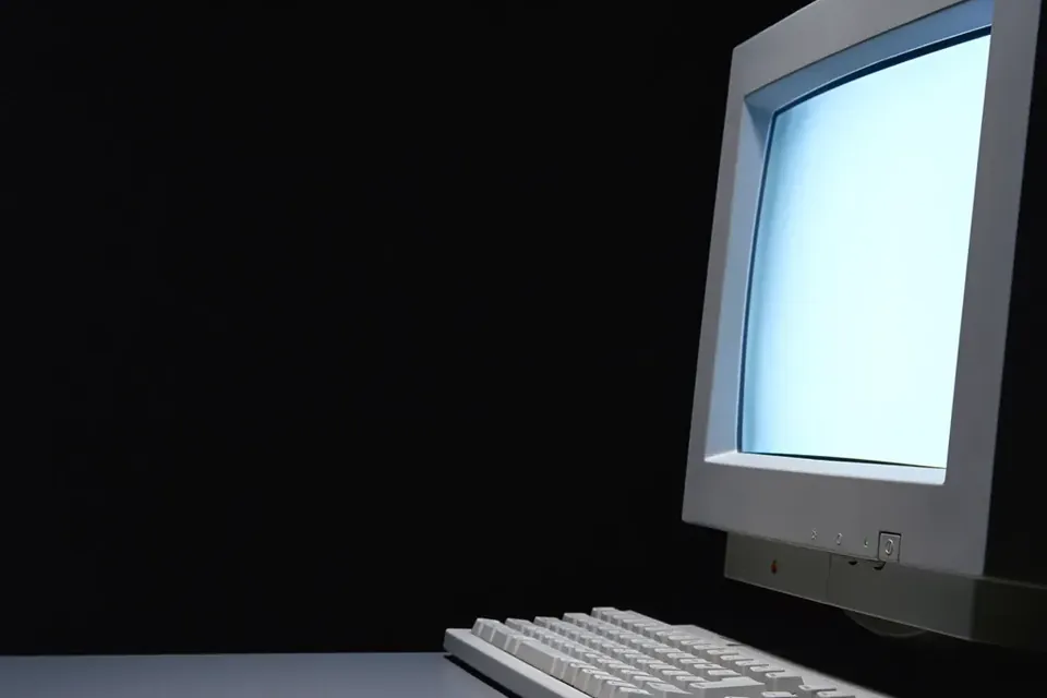 An old beige CRT monitor and keyboard in a dark room, the screen glowing